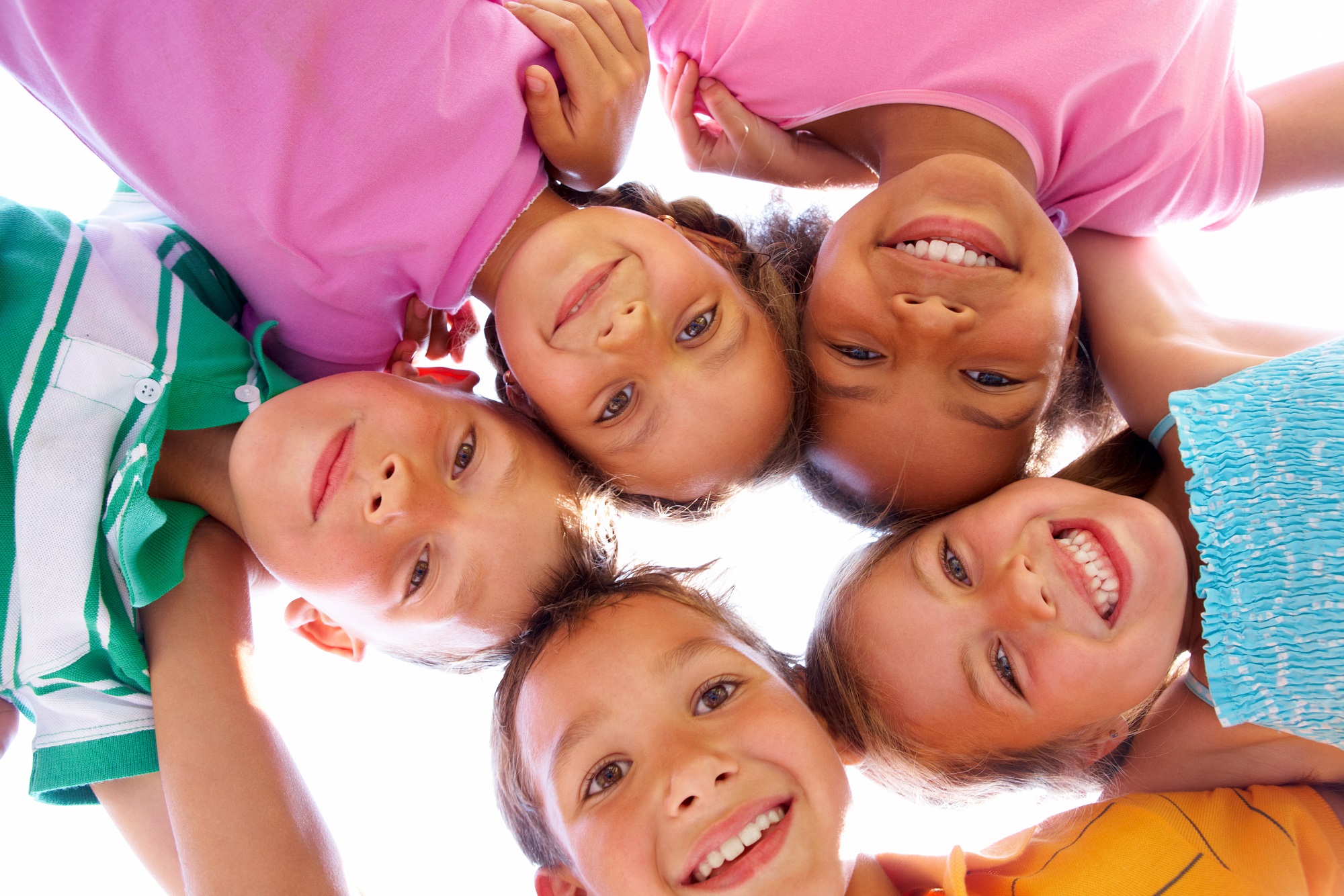 smiling children huddled together looking down over the camera in a circle