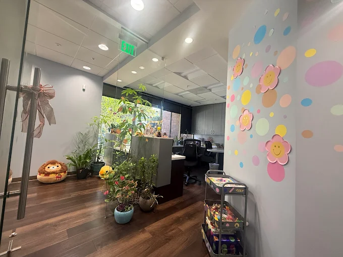 Front office photo. Grey walls with cute pink and yellow smiling flowers and polka dots on the wall. Lots of plants and large squishmellows in the lobby.