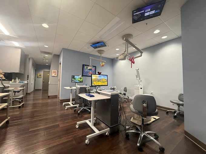 Exam room with stuffed animals hanging from the lights and tvs on the ceiling